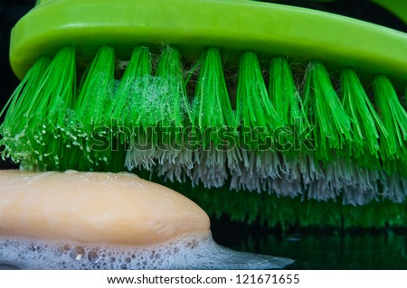 brush for washing hands and a piece of green soap with foam shot against a black background