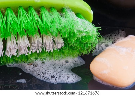 brush for washing hands and a piece of green soap with foam shot against a black background