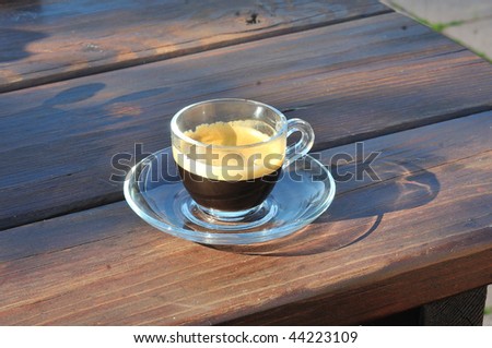 A cup made of clear glass with black coffee on a wooden table