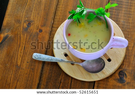 A big bowl of vegetable soup decorated with a sprig of parsley on the table in the garden