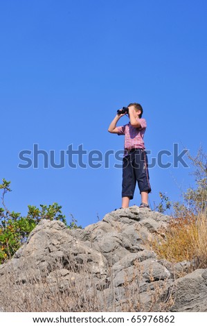 boy stands atop a mountain and sees the neighborhood through binoculars