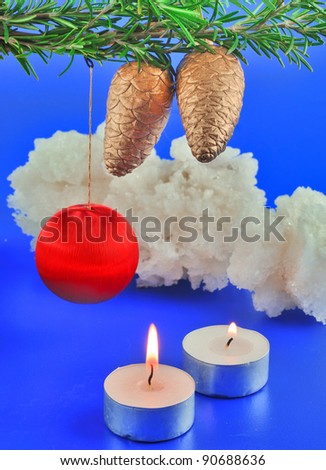 Red balls, cone spruce, ice and sprigs to decorate and candles burning for Christmas, against a blue background