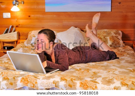 Girl with laptop lying on the bed in a rustic house and sends the mail to friends