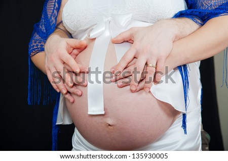 Pregnant woman put her arms around his stomach with both hands, and her husband put his hands on the arms of his wife