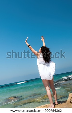 Girl with a white cape on a cliff above the sea raised her hands to heaven