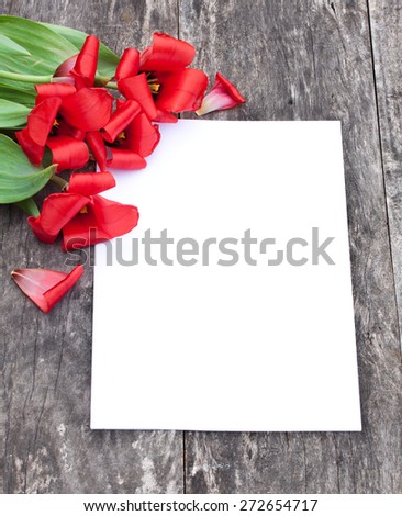 faded red tulips on the oak brown table with white sheet of paper