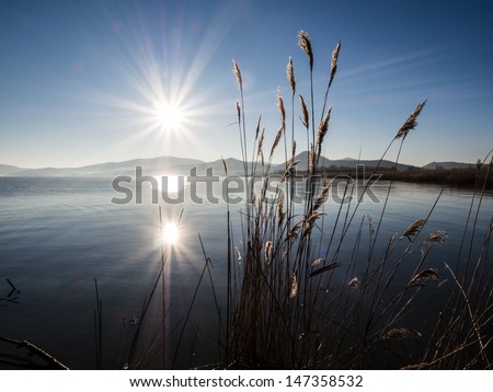 Sun reflected in the lake on sunrise over mountains with spikes