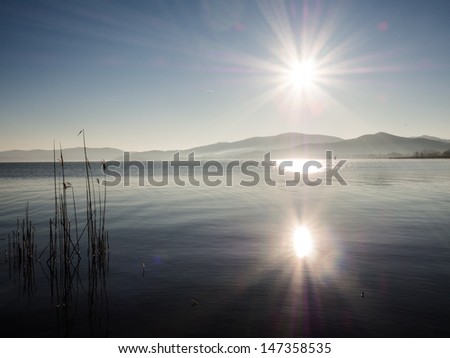 Sun reflected in the lake on sunrise over mountains with spikes