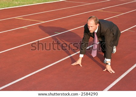 Business man on a red running track in the start position ready to run