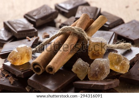 Chocolate with cinnamon sticks and piece of brown sugar on coffee background, selective focus