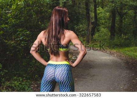 Image of athletic young woman rubbing the muscles of her lower back after jogging in park