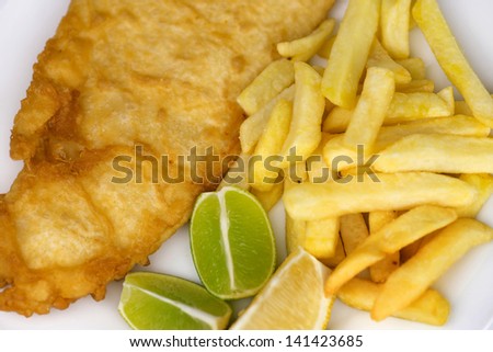 Salted french fries with large serving of fried fish with lemon and lime wedges