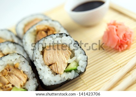 Closeup of teriyaki chicken sushi rolls with cucumber, chopsticks, ginger and soy sauce