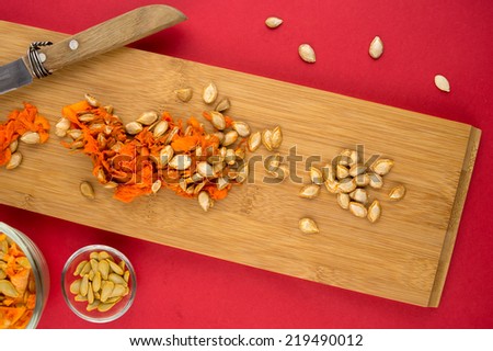 Wooden cutting board with orange squash seeds against red background