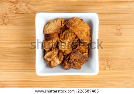 Dehydrated pineapple chunks in a white bowl on wooden background
