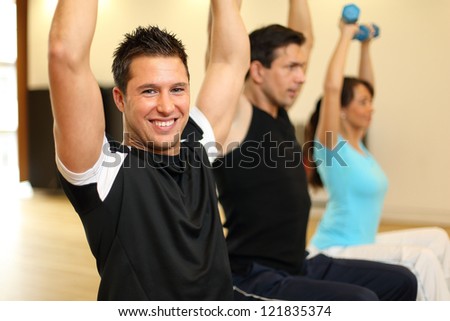 Two men and one woman exercising with dumbbells on gymnastics balls