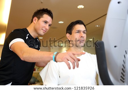 Personal trainer in a gym showing athletic man the training bike