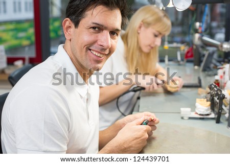 Dental technician in a lab polishing gold tooth and smiling into the camera