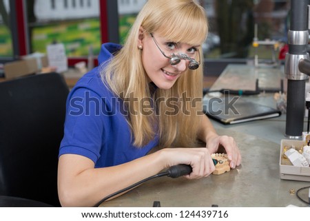 Dental technician with surgical loupes polishing gold tooth in a laboratory