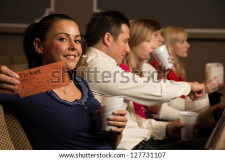 A woman in the audience of a theater, in a concert hall or a cinema presenting a ticket or admission pass