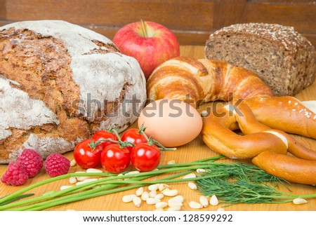 Different types of food such as bread, a tomato, apple, pine seeds, raspberry and a pretzel