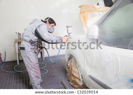 Car body painter spraying paint or color on bodywork in a garage or workshop with an airbrush
