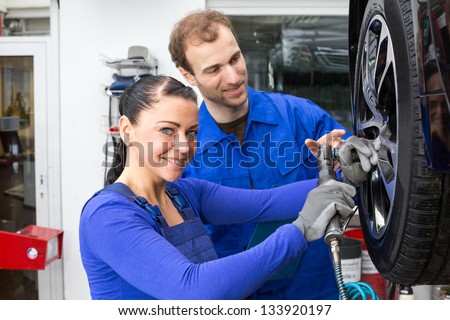 Two mechanics changing a wheel on a car standing on a hydraulic ramp