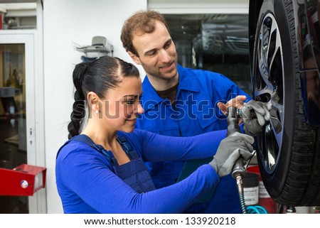 Two mechanics changing a wheel on a car standing on a hydraulic ramp