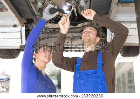 Two mechanics repairing or inspecting a car on hydraulic lift