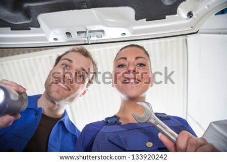 Two mechanics taking a look under the hood of a car in a garage to repair it