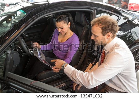 Car salesman sells a car to happy customer in car dealership and hands over the keys.