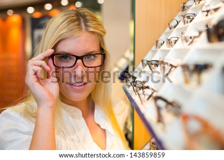 Customer in optician\'s shop choosing the right frame for eyeglasses from a shelf with many different models