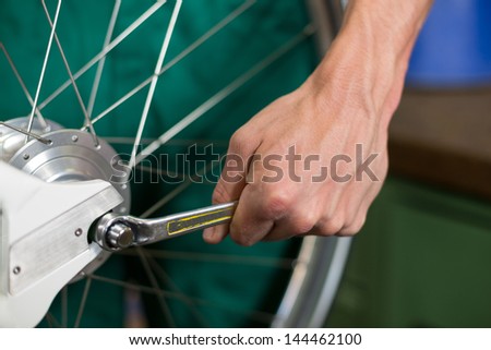 Closeup of bicycle mechanic with a wrench repairing bike wheel
