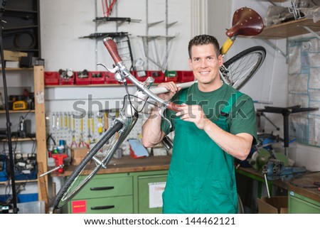 Bicycle mechanic carrying a bike in workshop smiling into the camera