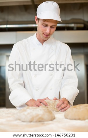 Baker kneading bread dough in bakery on a table at the oven
