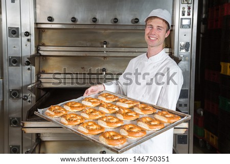 baker posing with baking tray full of pretzels in front of the oven