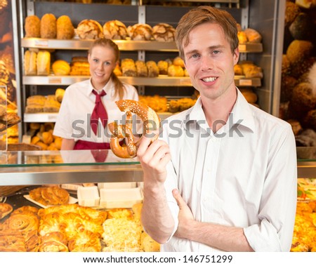 Happy customer holding a pretzel inside a bakery with the shopkeeper standing in background