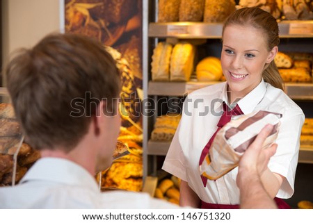 Shopkeeper in bakery or baker\'s shop selling bag full of bread to customer
