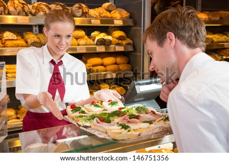 Shopkeeper in bakery or baker\'s shop presenting tablet with sandwiches, cold cut, cheese, cold meat and egg.