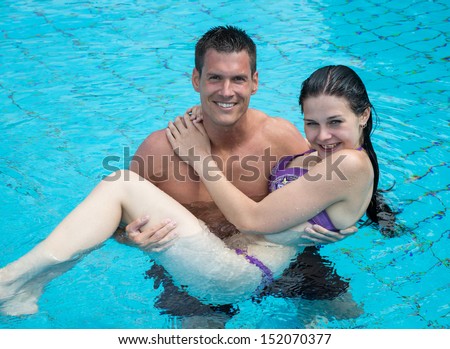 Man carrying his girlfriend in the water at public swimming pool