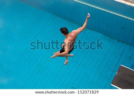 Man jumping from diving board at public swimming pool