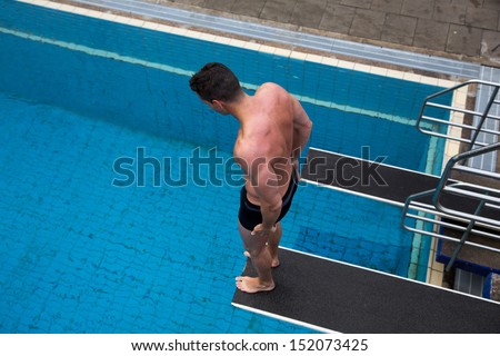 Man with fear of height standing on diving board at public swimming pool above the water