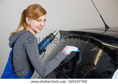 Female worker tinting car window in garage with a tinted foil or film