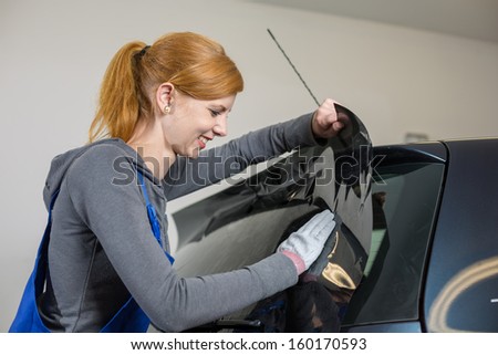 Car wrappers tinting a vehicle window with a tinted foil or film using heat gun and squeegee