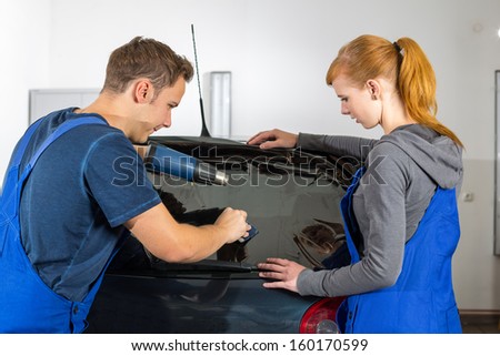 Worker In Garage Tinting A Car Window With Tinted Foil Or Film