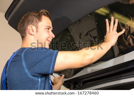 Worker in garage tinting a car window with tinted foil or film