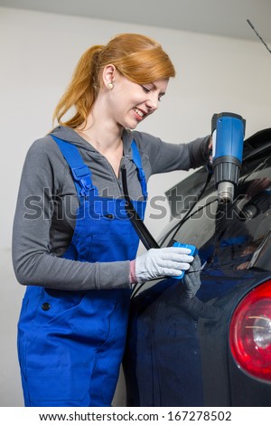 Female worker tinting car window in garage with a tinted foil or film