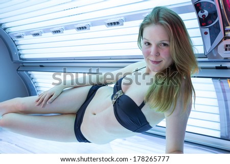 Happy woman in bikini on tanning bed in solarium
