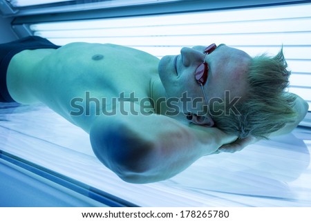 Attractive man in solarium enjoying sunbathing on tanning bed