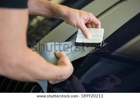 Car wrapper straightening wrapping foil with a squeegee to remove air bubbles